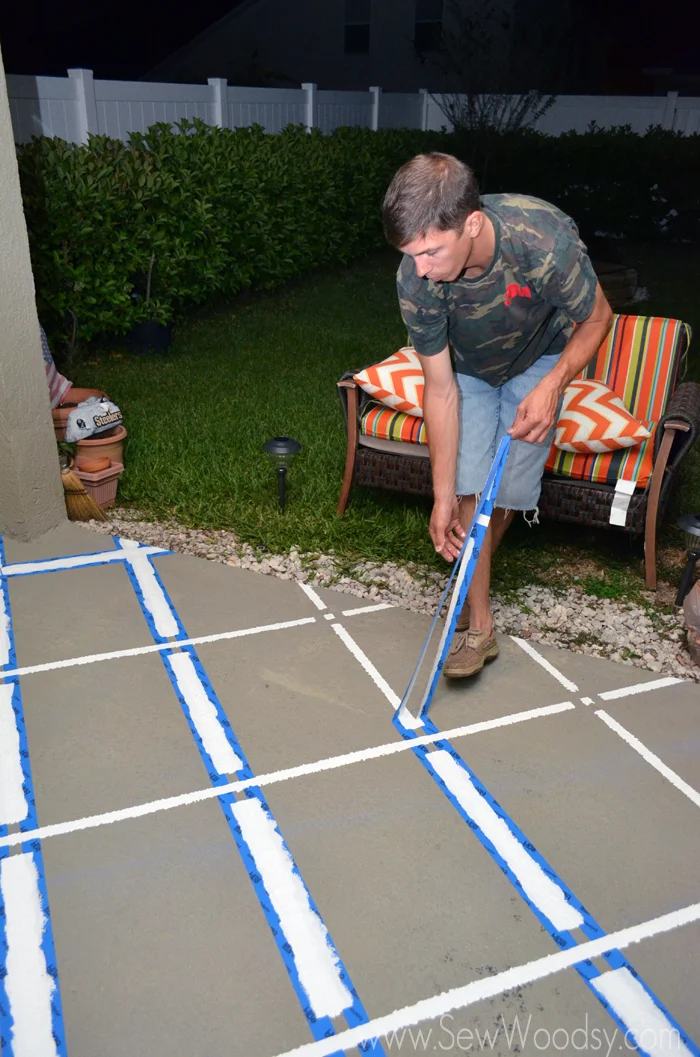 Man pulling painters tape off patio revealing paint pattern.