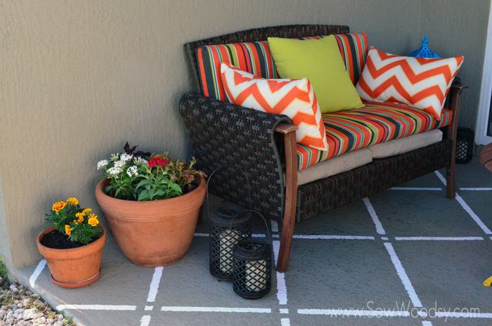 Rattan couch with brightly covered cushions, pots with flowers, lanterns, and stripes painted on floor.