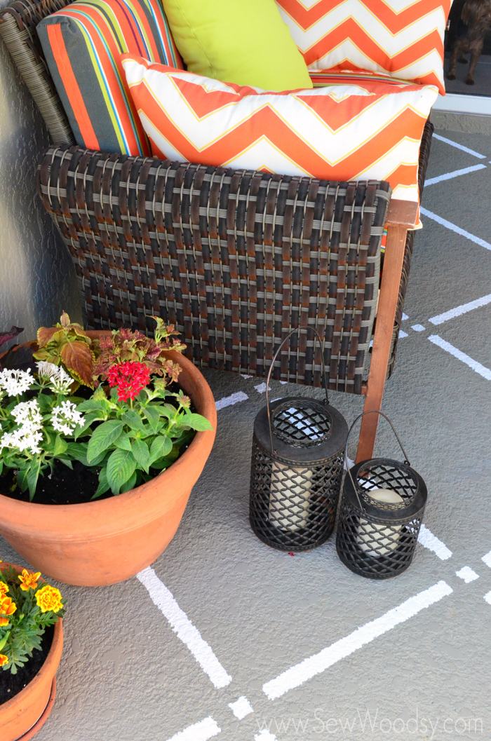 Outdoor couch with orange cushions, plants in planters, lanterns, and pattern painted on floor.