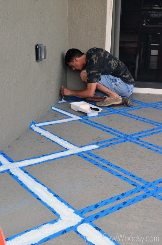 Man using a paint brush painting blue painters tape on a patio.