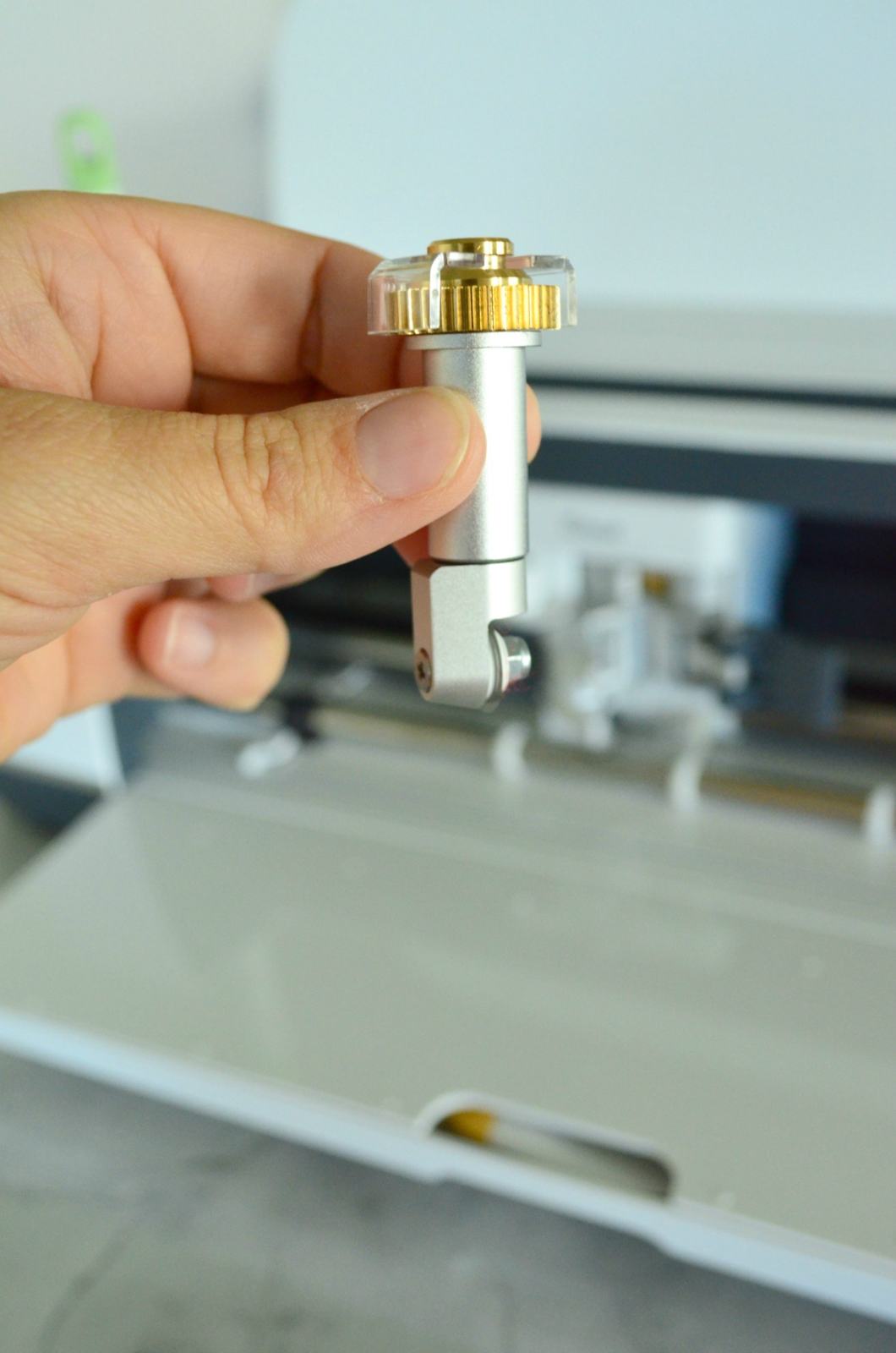 Female hand holding a Cricut Maker Rotary Blade with Cricut Maker in the background.
