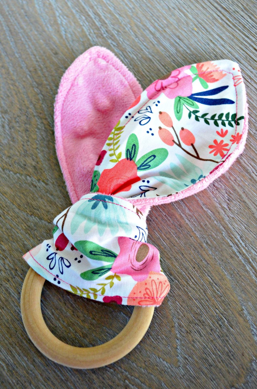 Wooden teething ring with pink and floral fabric tied around it.