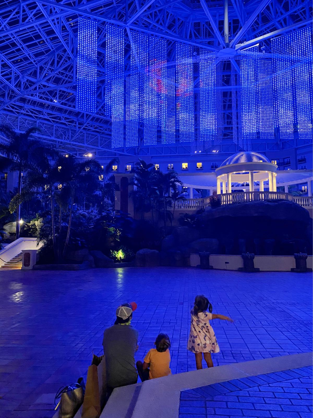 Father and children sitting on steps watching light show in a hotel.