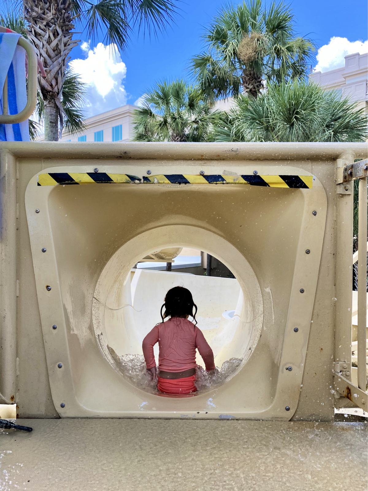 Little girl sliding down on her bottom on a water slide.
