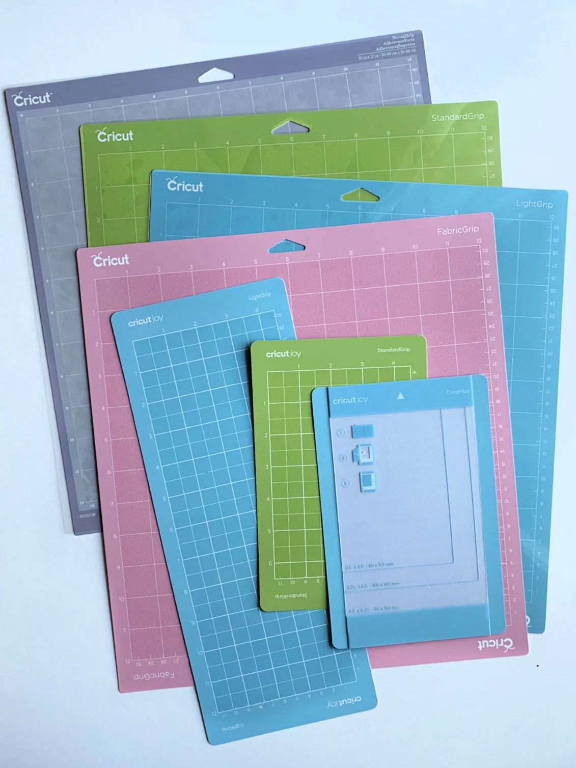 7 different Cricut Mats in green, blue, pink, and purple on a white a surface.