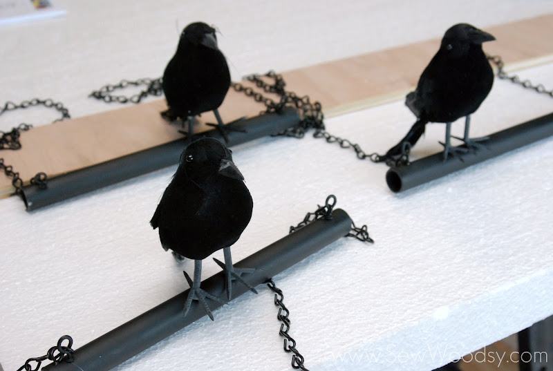 Three black PVC pipes with chains with crows sitting on top of it all sitting on top of white foam.