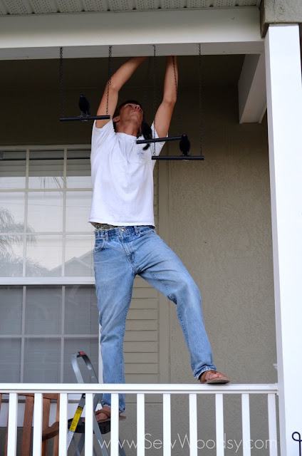 Man standing on a step stool and porch railing hanging crows.