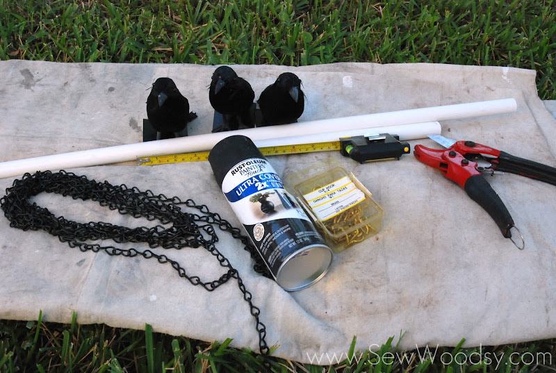 Tan drop cloth with fake crows, black chain, black spray paint, tape measure, hooks, PVC cutters, and PVC pipes.