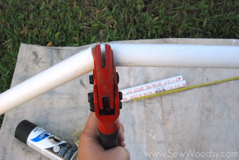 Hand holding PVC cutters, to cut PVC pipe over a tan drop cloth.