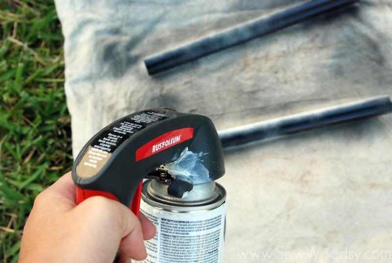 Hand holding Rust-Oleum spray paint can spraying PVC on a cream drop cloth on the grass.