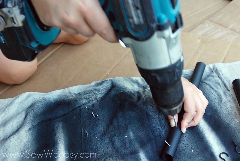 Hand holding a piece of PVC and drilling a hole in the PVC.