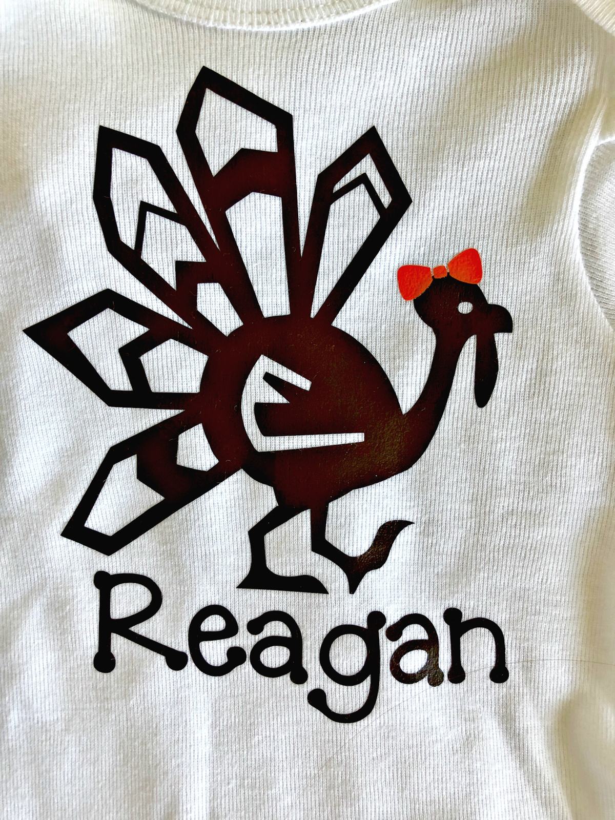 Close up of a turkey shirt with an orange bow and name "reagan" on it.