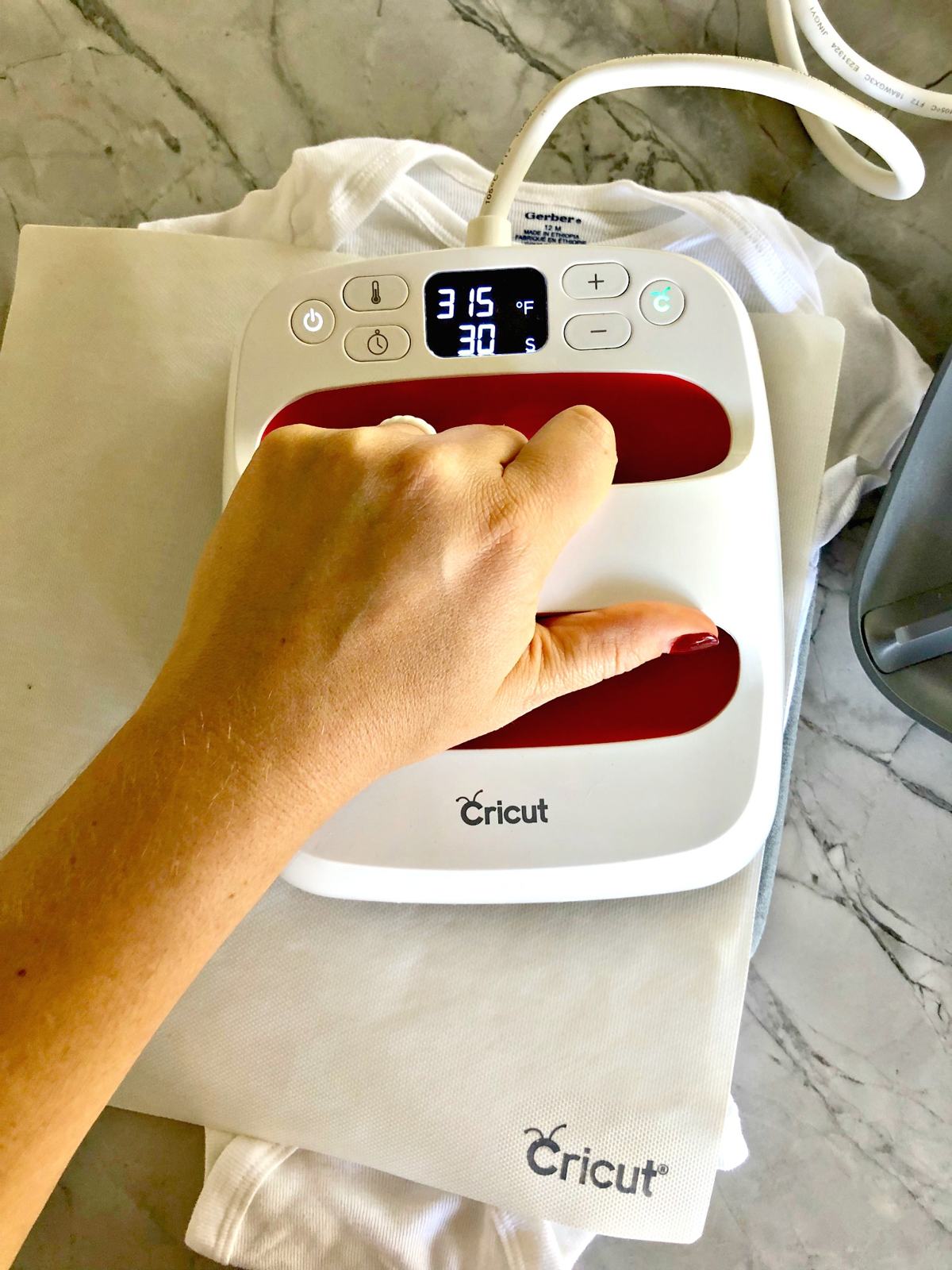 Top view of a female hand using an EasyPress Mini on a baby onesie.