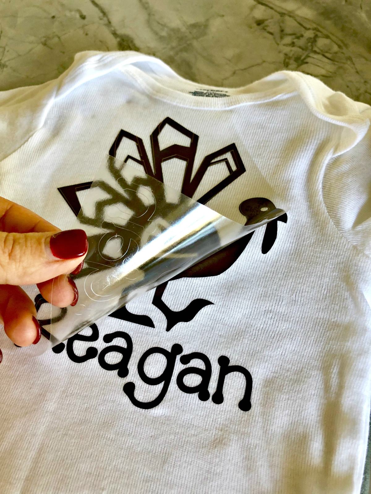 Female hand with maroon nails pulling of the plastic to iron on vinyl on a tshirt.