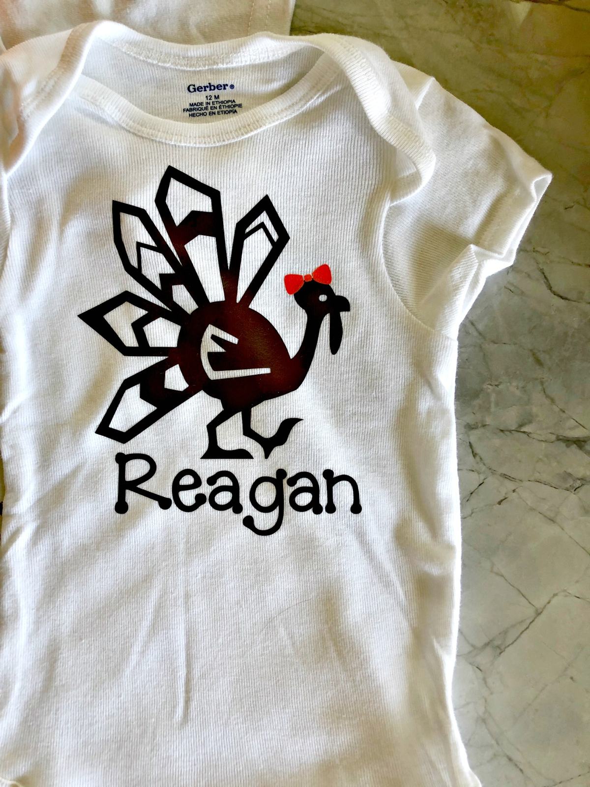 Top view of a white onesie with a turkey with an orange bow on it with name on shirt.