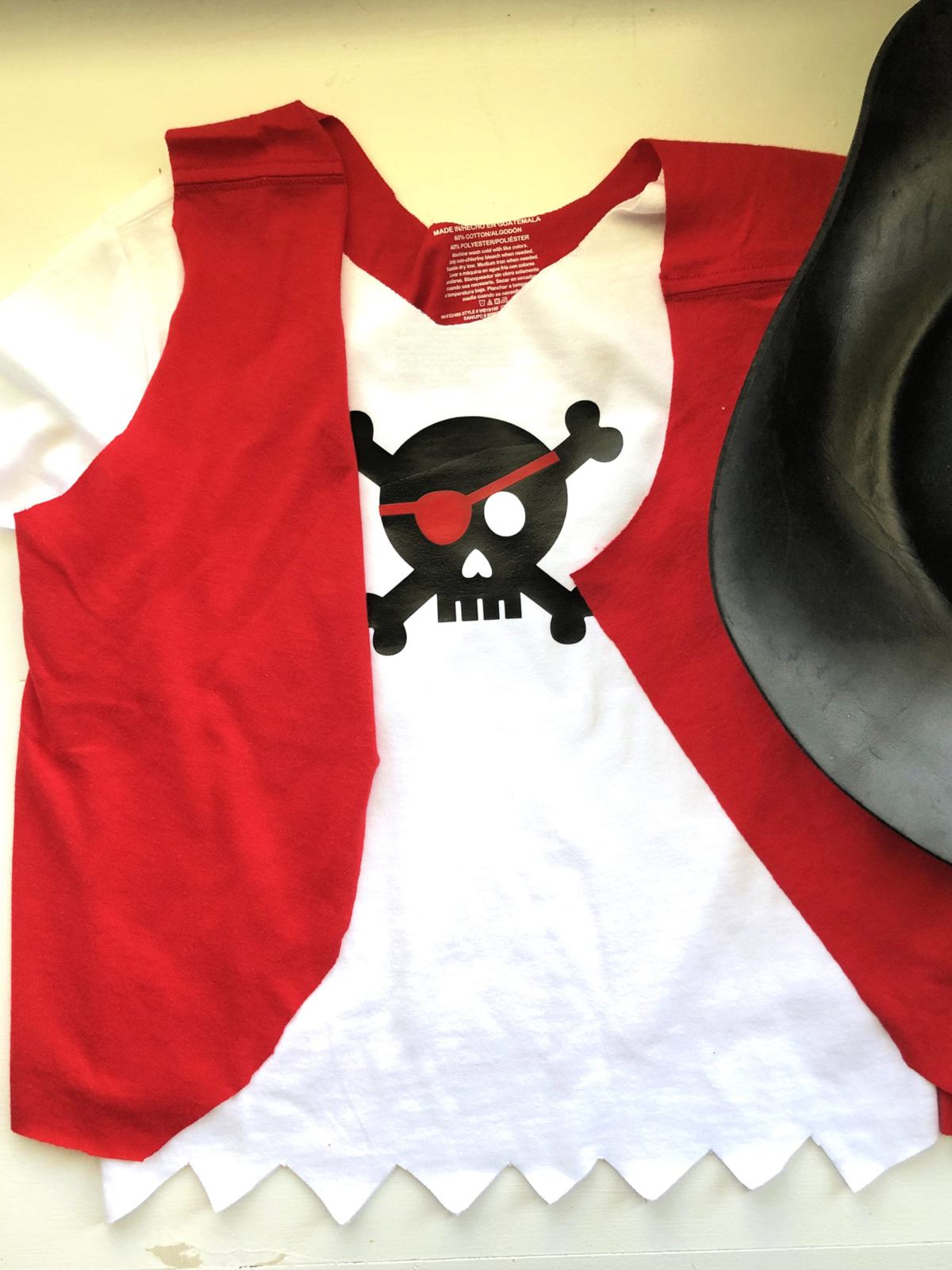 White shirt with black skull and red cloth vest with black hat.