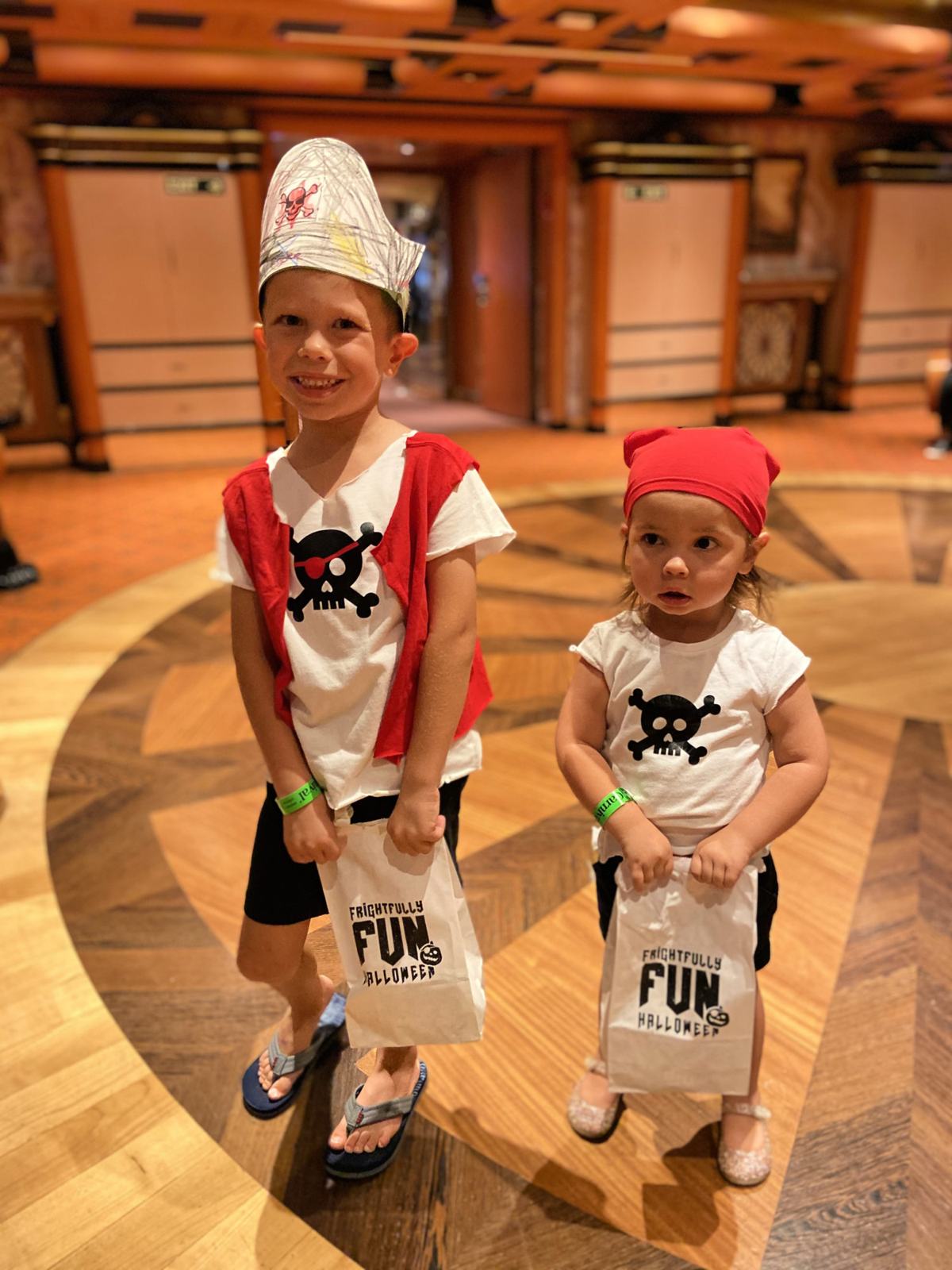 brother and sister dressed up with pirate shirts holding white paper bags.