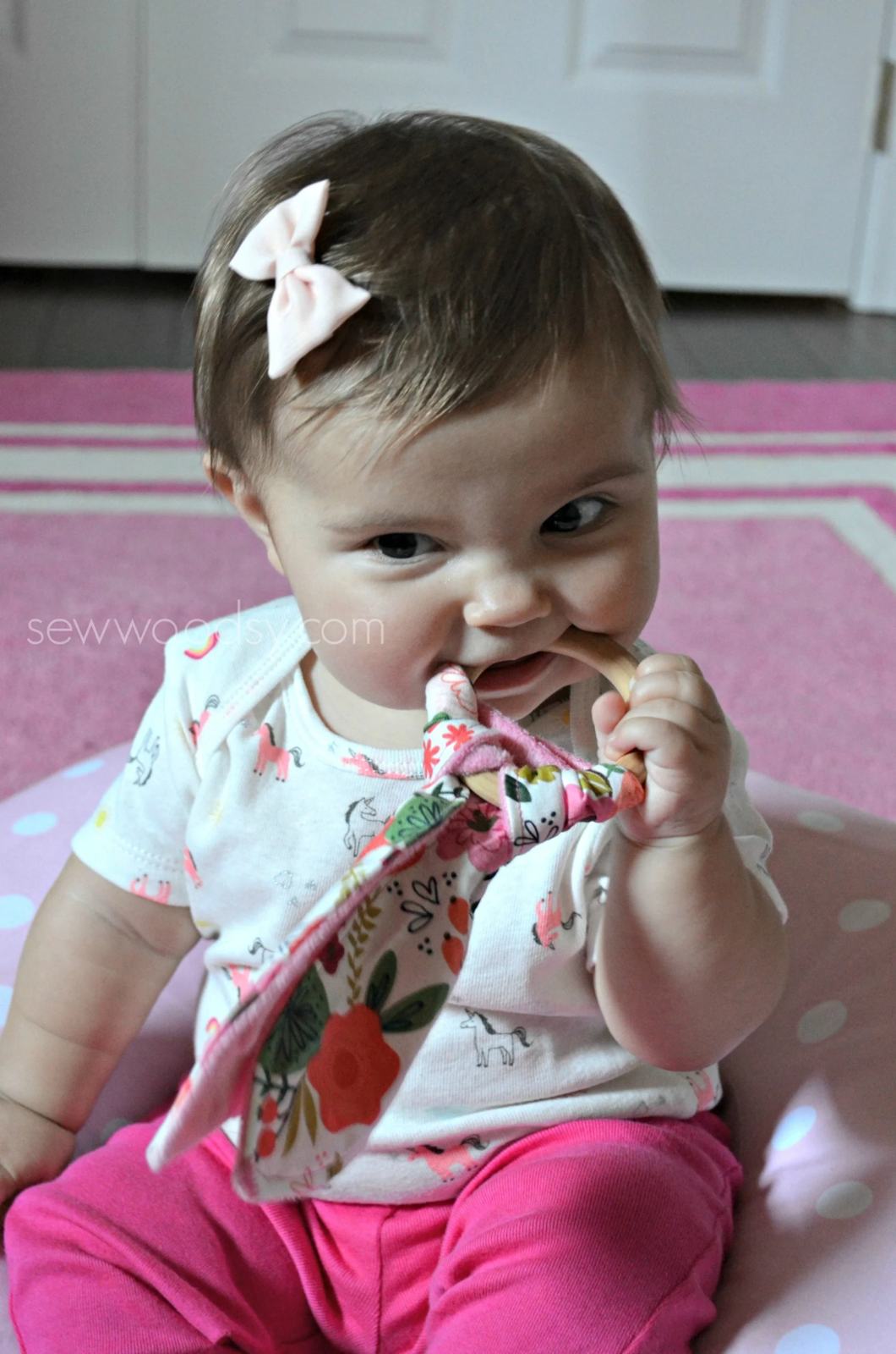 Baby girl chewing on a wooden teething ring.