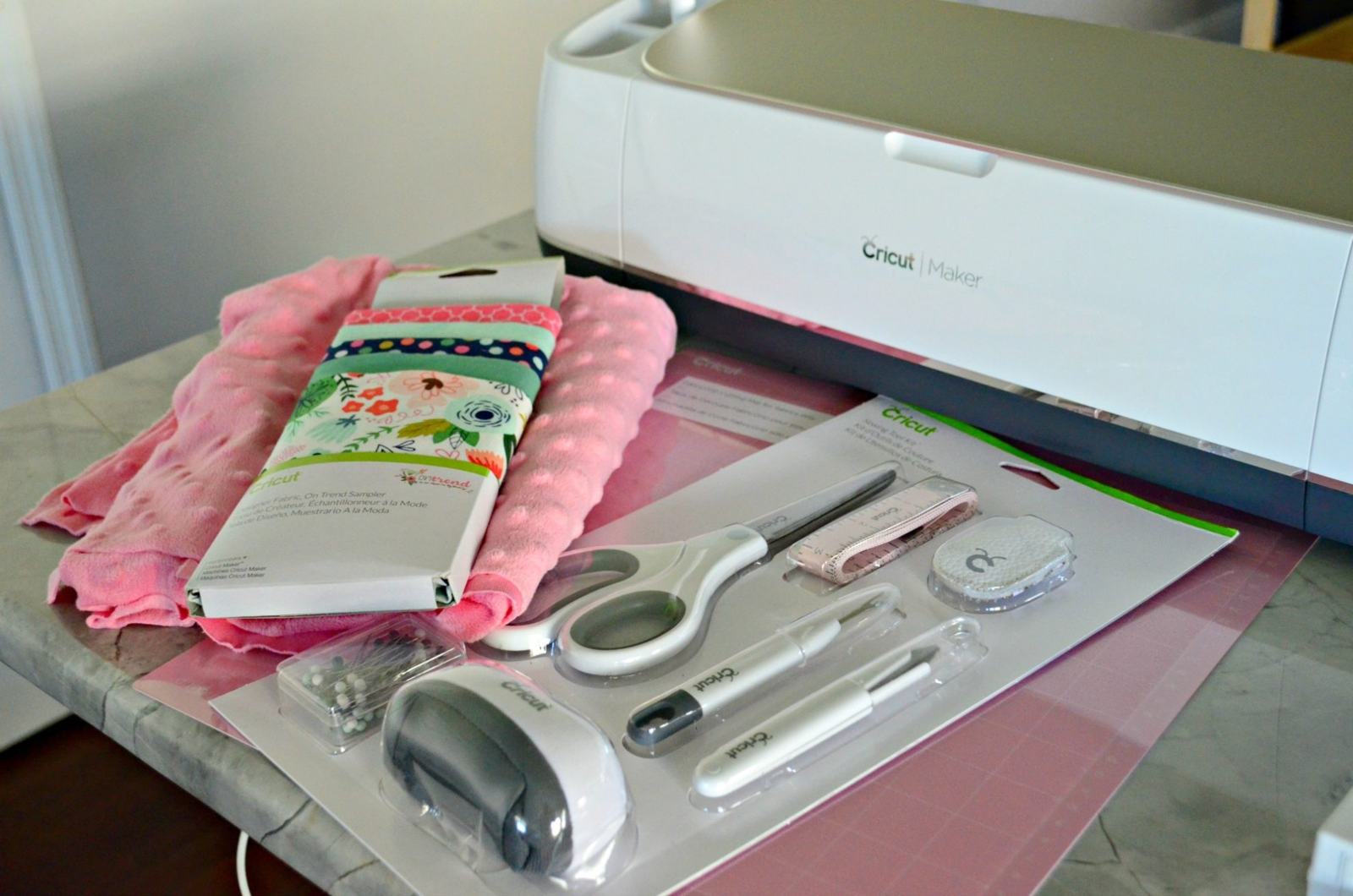 supplies on countertop: fabric, Cricut Maker, pink mat, and sewing supplies.
