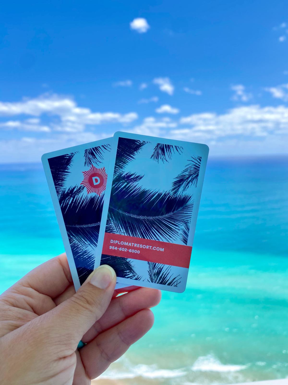 Female hand holding two hotel keys overlooking the ocean.
