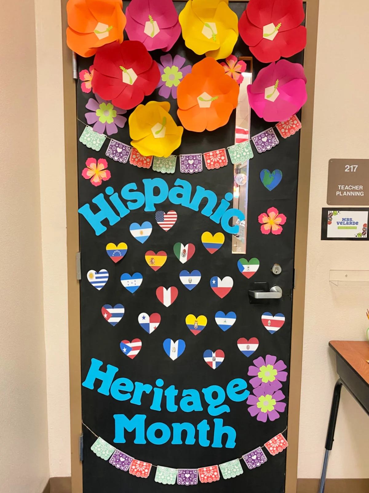 Black classroom door with the words "Hispanic Heritage Month" with hibiscus flowers and hearts of country flags.