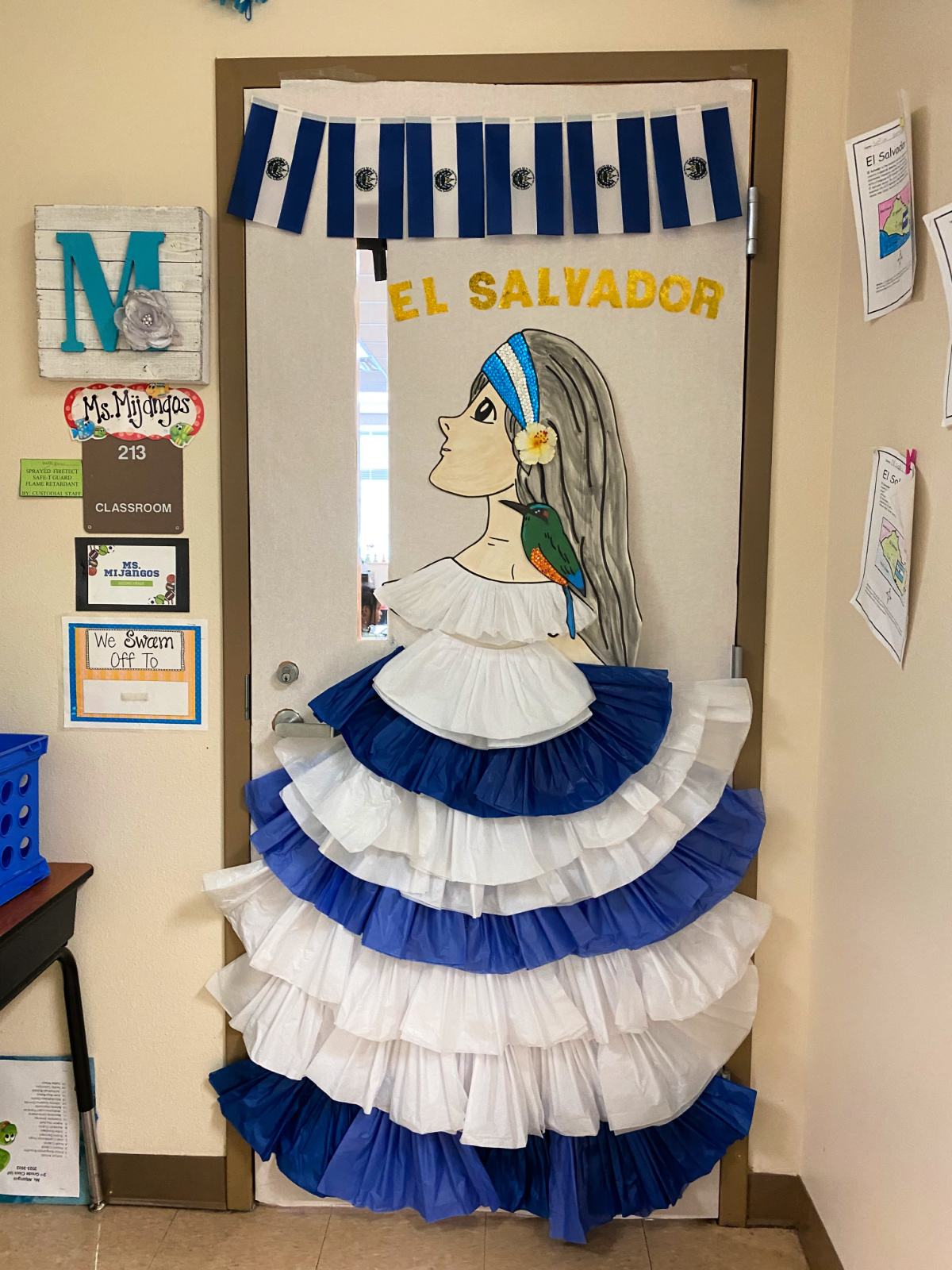 White classroom door with a female in a white and blue dress with the words "El Salvador" on the door.