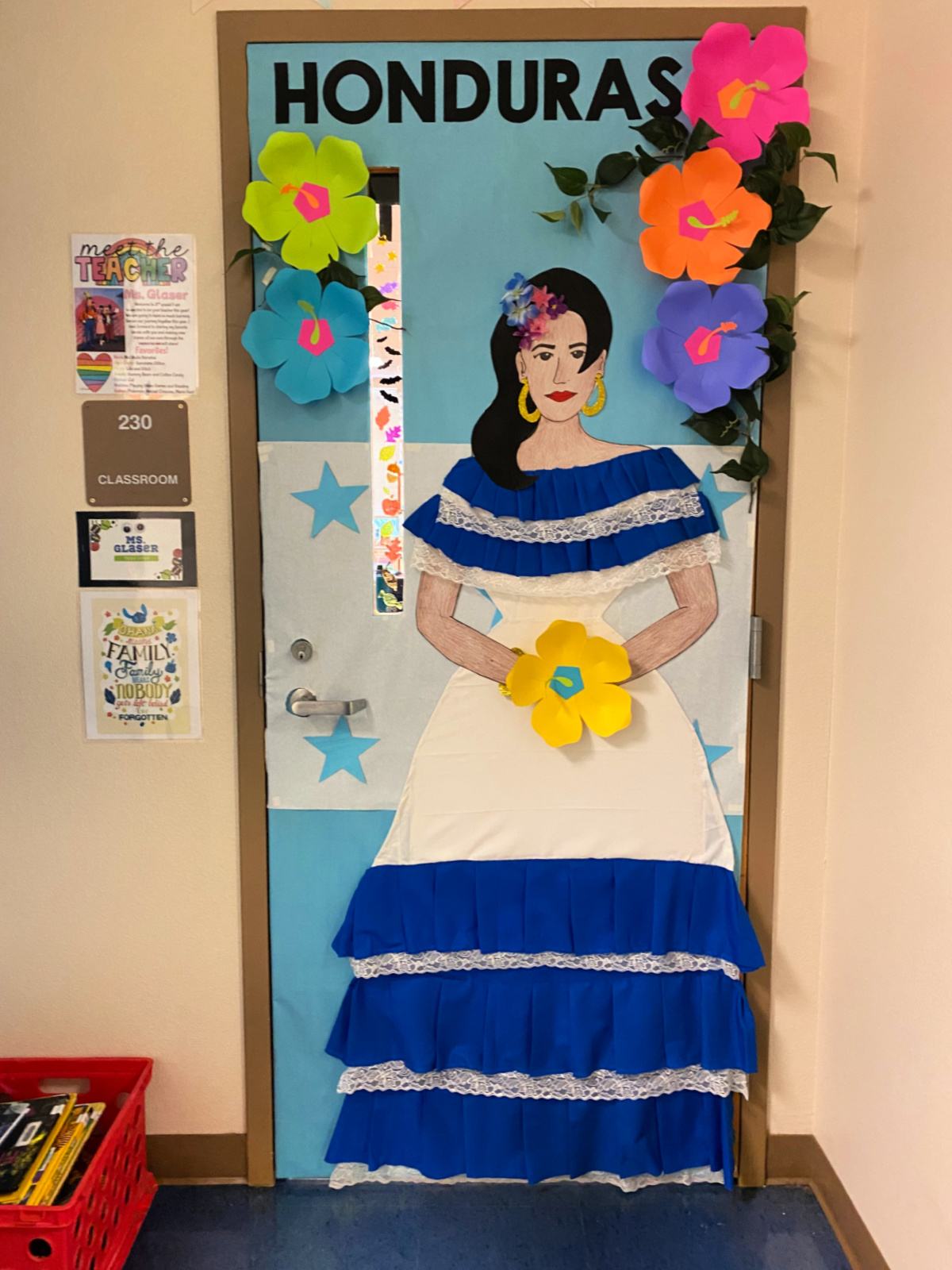Classroom door with a female in a white and blue dress with the Honduras flag and tropical hibiscus flowers.