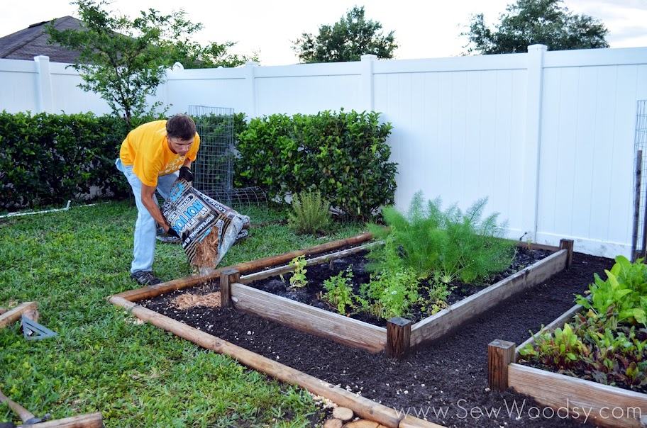 Man in yellow shirt pouring mulch in a garden bed.