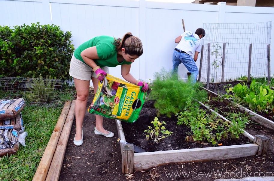 Female pouring Miracle Gro Garden Soil in a planter bed.
