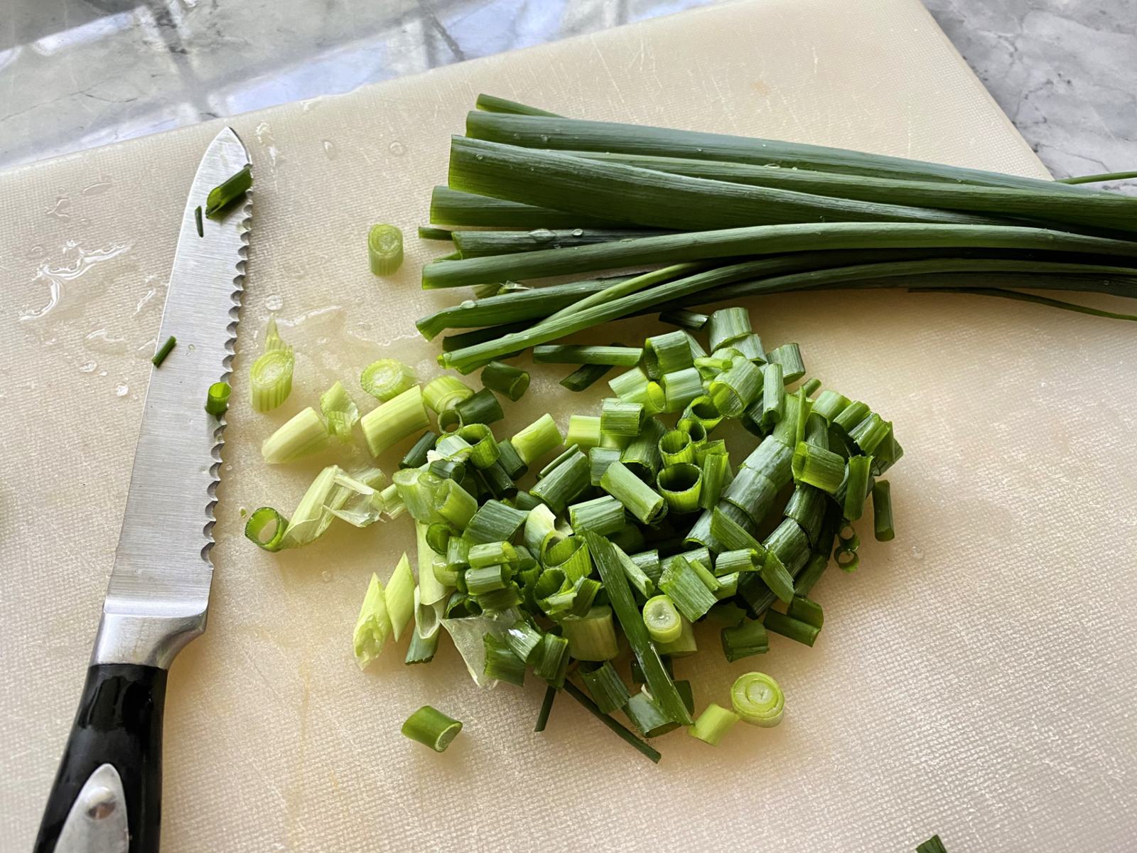 White cutting board with serrated knife with green onion stalks and sliced pieces.