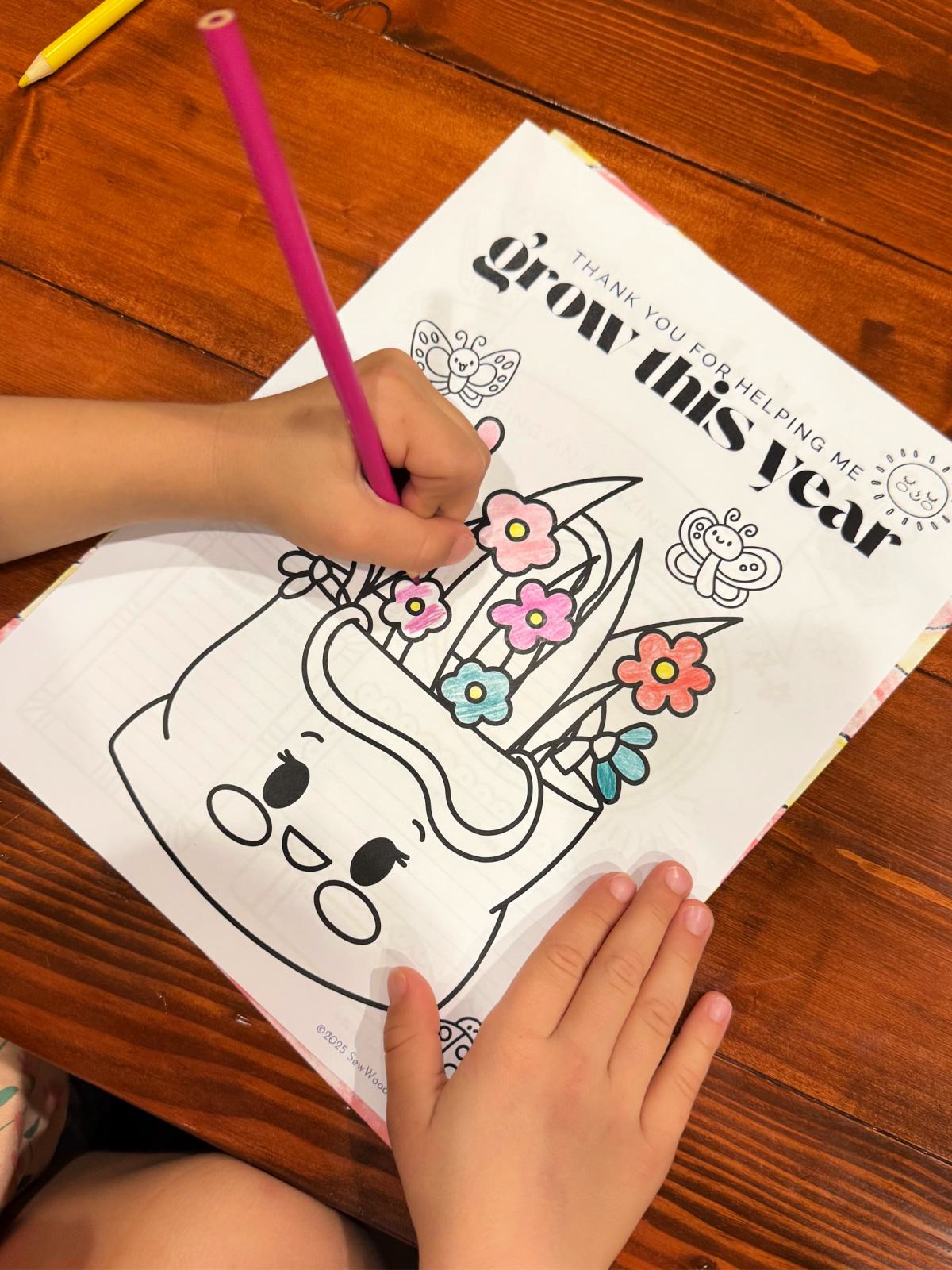 Little girl coloring a plant coloring page on a wood table.
