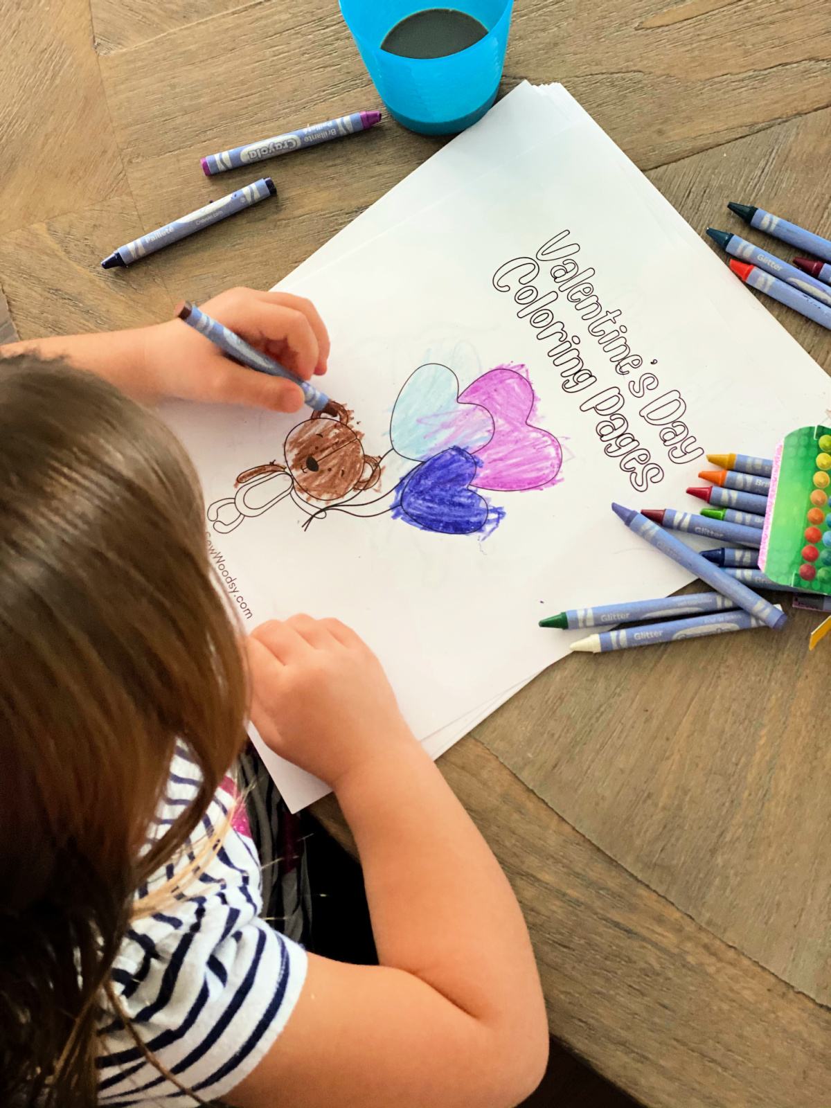 little girl coloring a bair brown holding balloons with crayons scattered on table.