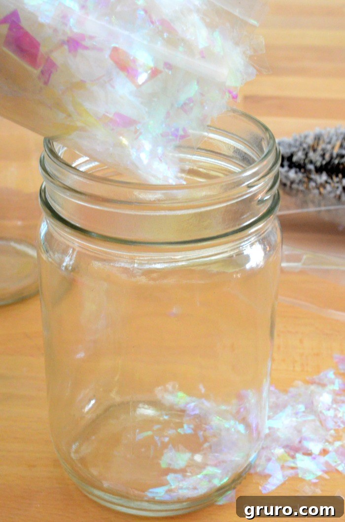 A bag of fake sparkling snow being carefully poured into a clear mason jar, filling it about one-quarter full to create a snowy base.