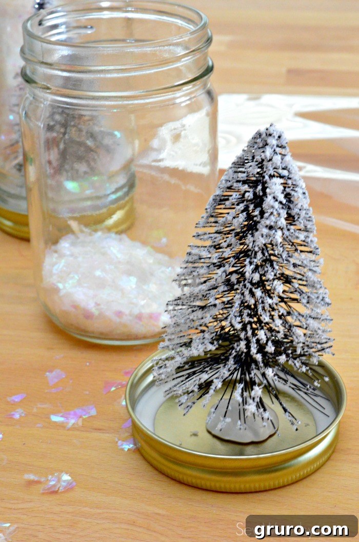 A miniature wire bottle brush Christmas tree is firmly secured with a glue dot to the inside center of a silver mason jar lid, ready for assembly.