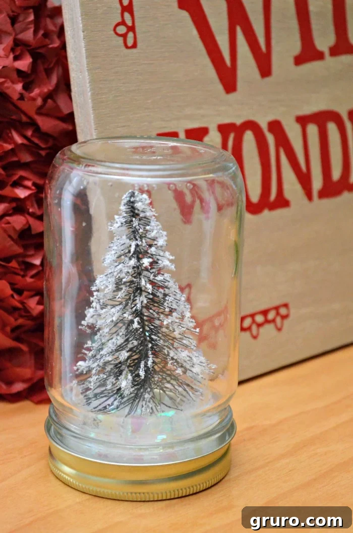 A completed Christmas Tree Mason Jar, featuring a miniature tree enveloped by sparkling fake snow, proudly displayed on a rustic wooden table.