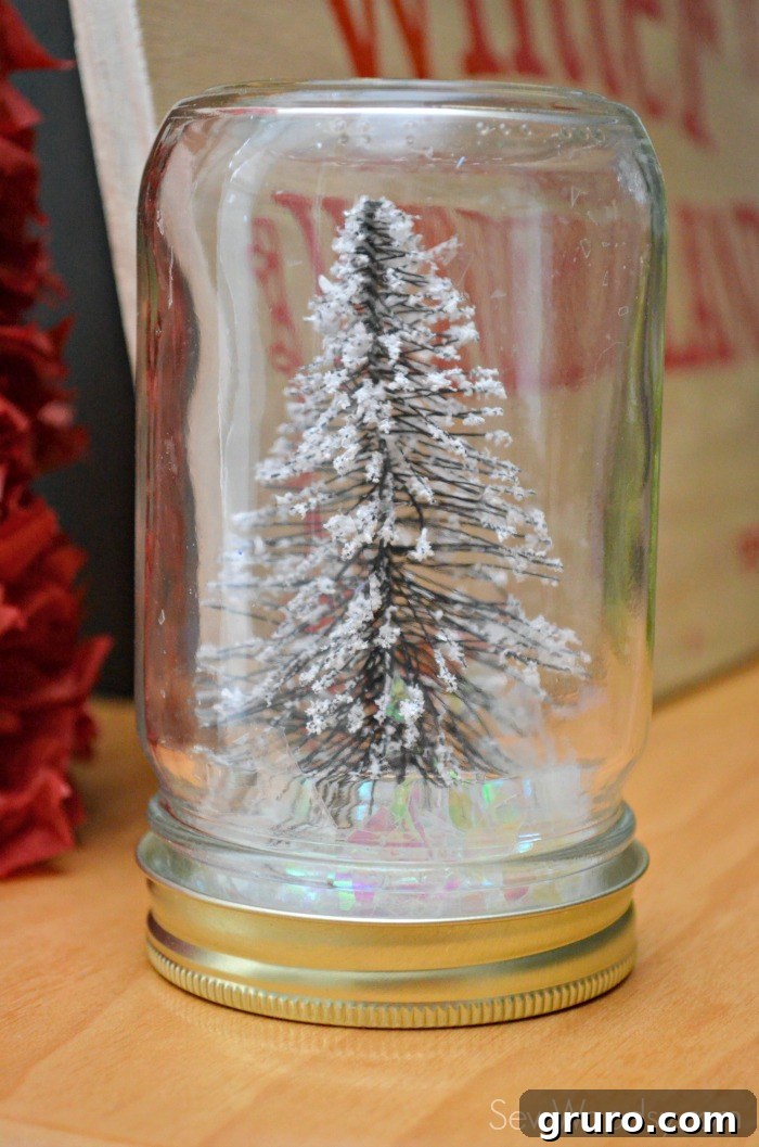 Close-up of a beautifully crafted Christmas Tree Mason Jar, showcasing a miniature tree amidst sparkling fake snow, ready for holiday display.