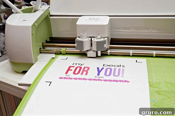 Pitter-Patter Valentine: Classroom Edition 6 A Cricut machine actively cutting a colorful Valentine card placed on a green cutting mat.