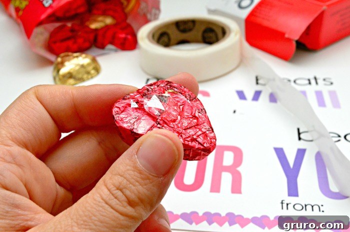 Pitter-Patter Valentine: Classroom Edition 7 A hand holding a Reese's Heart candy with a small glue dot sticker attached to its back.