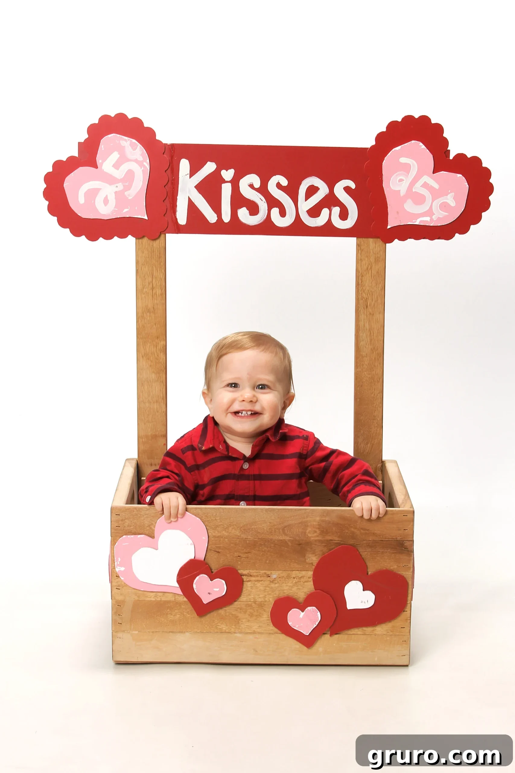 Romance in Focus 4 Little baby boy sitting in a kissing booth made out of a wood crate with hearts stapled on front, looking adorable.