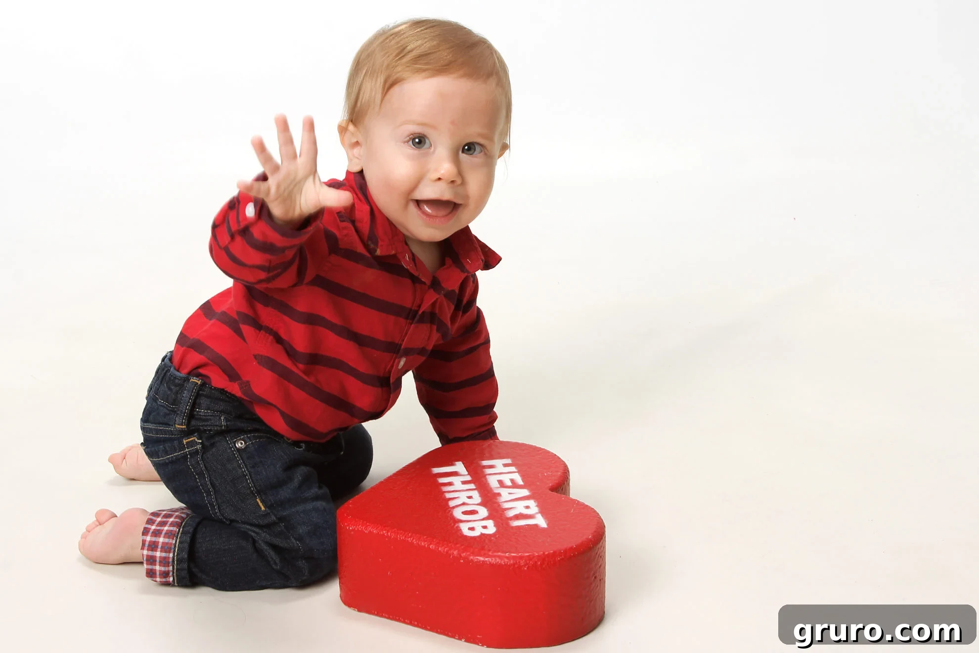 Romance in Focus 6 Little boy baby on knees waving at the camera with other hand on a heart throb heart prop.