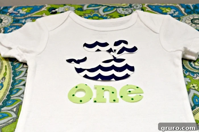 Placing the fabric 'ONE' design onto a baby onesie for optimal positioning before ironing