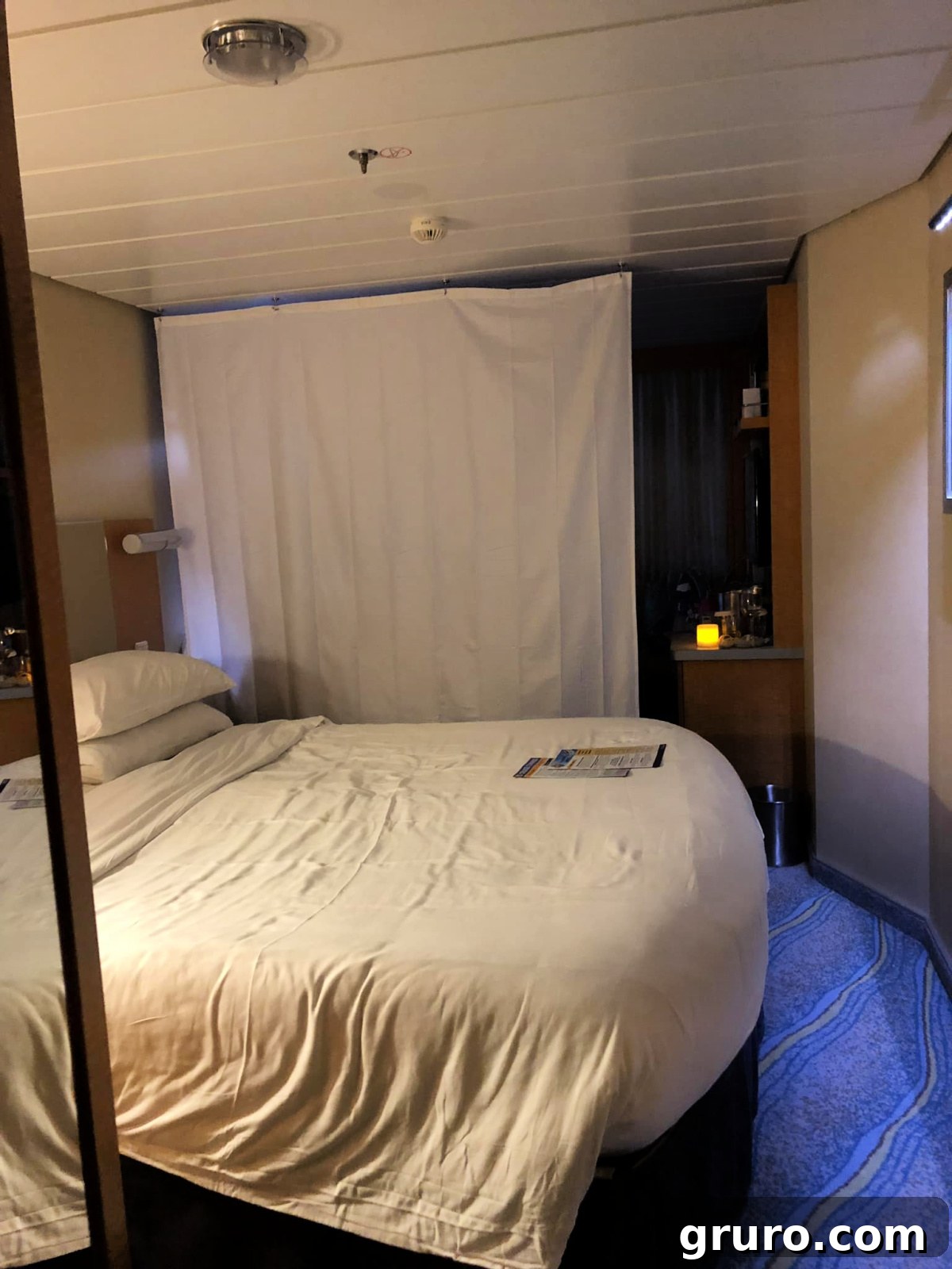 A white curtain effectively dividing two areas of a small cruise ship room, enhancing privacy and creating separate spaces.