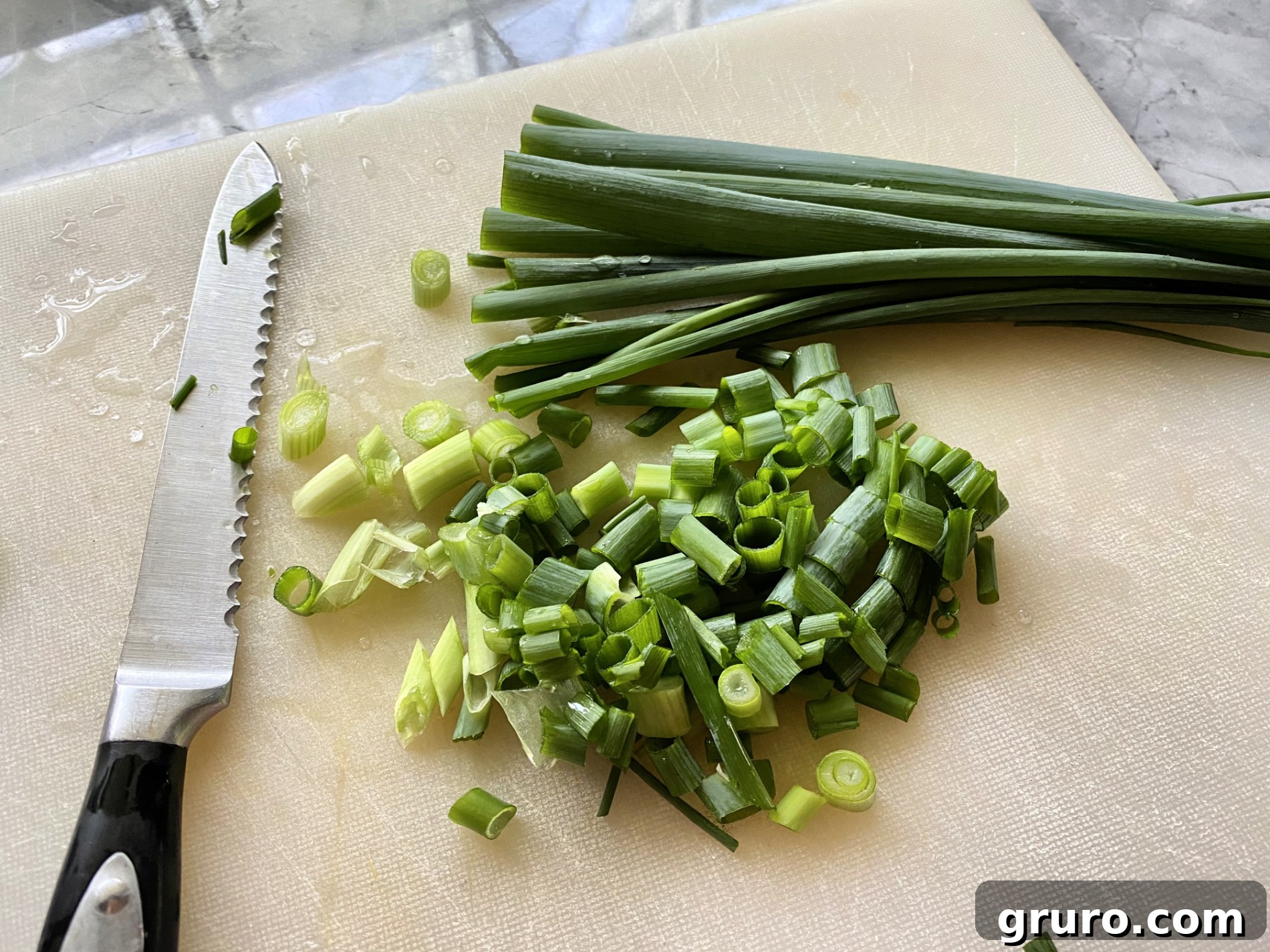 White cutting board with serrated knife with green onion stalks and sliced pieces.