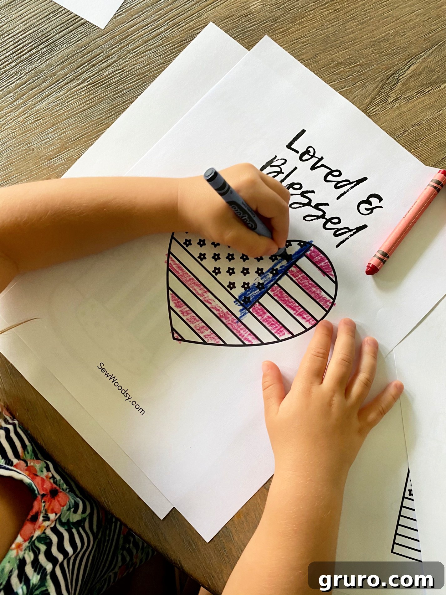Top view of a little girl coloring an American Flag heart with text on paper that reads "Loved & Blessed".