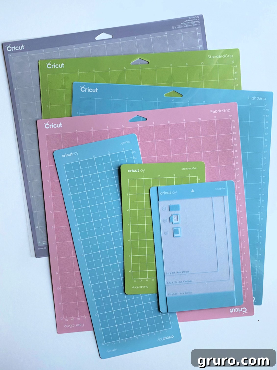 Seven different color-coded Cricut Mats, including green, blue, pink, and purple, arranged on a white surface, showcasing their variety and distinct uses.