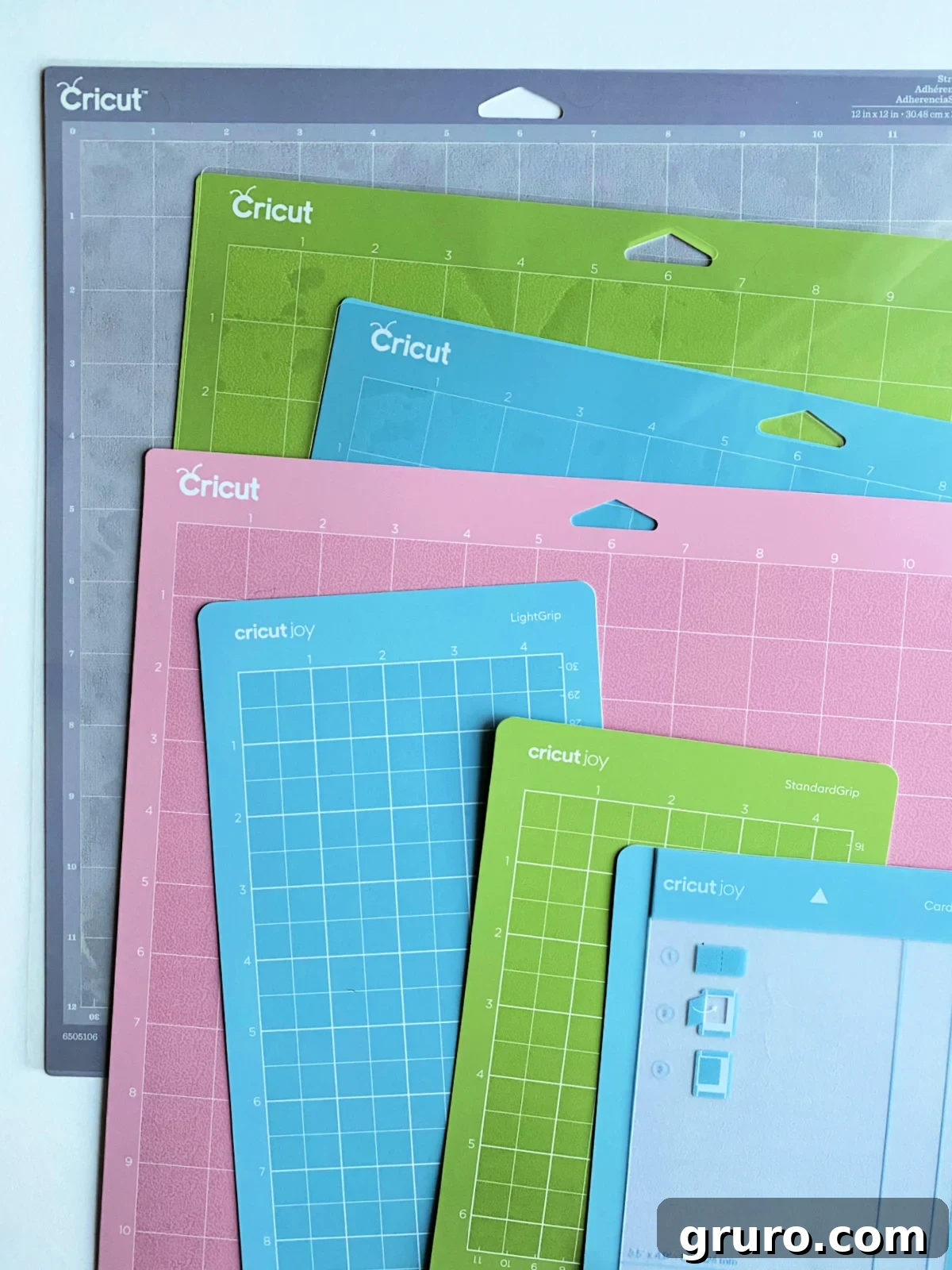 A collection of seven Cricut mats, ranging in various sizes and grip strengths, are artfully layered on a crisp white table, ready for crafting.