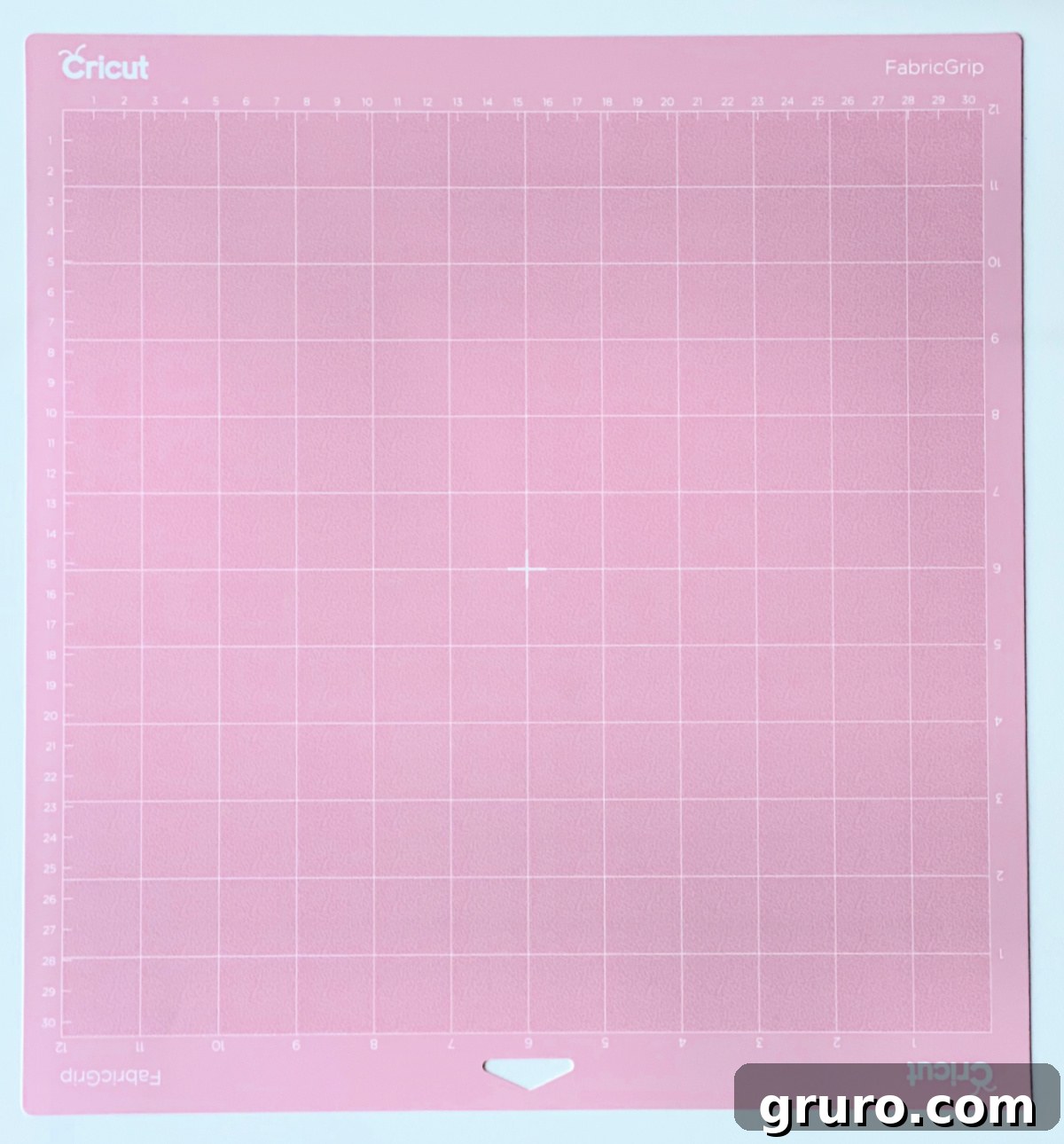 A soft light pink Cricut FabricGrip Mat positioned on a clean white surface, indicating its specialized use for delicate and intricate fabric cutting projects.