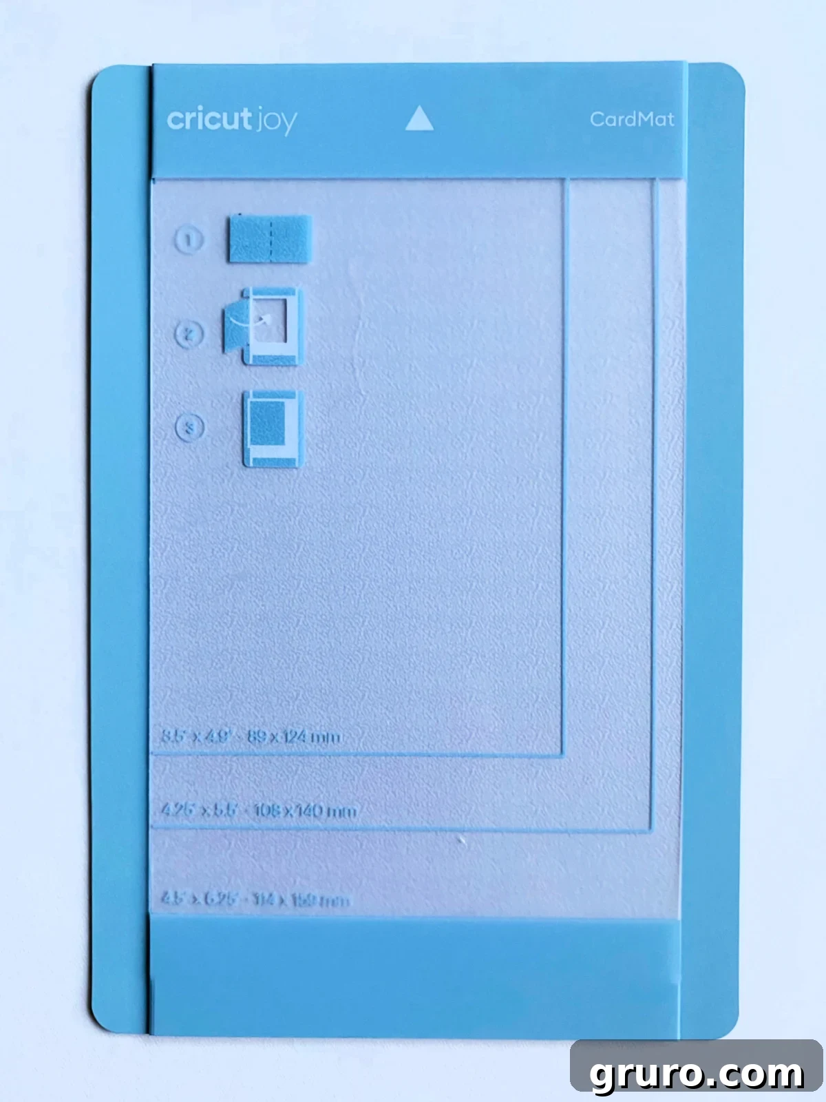 A small, light blue Cricut Joy Card Mat, designed for precise card-making, rests on a white surface, showcasing its unique folded design.