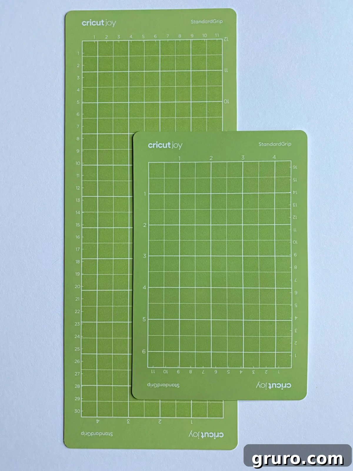 Two bright green Cricut Joy StandardGrip mats, varying in length, are arranged on a white surface, indicating their versatility for standard materials with the Cricut Joy.