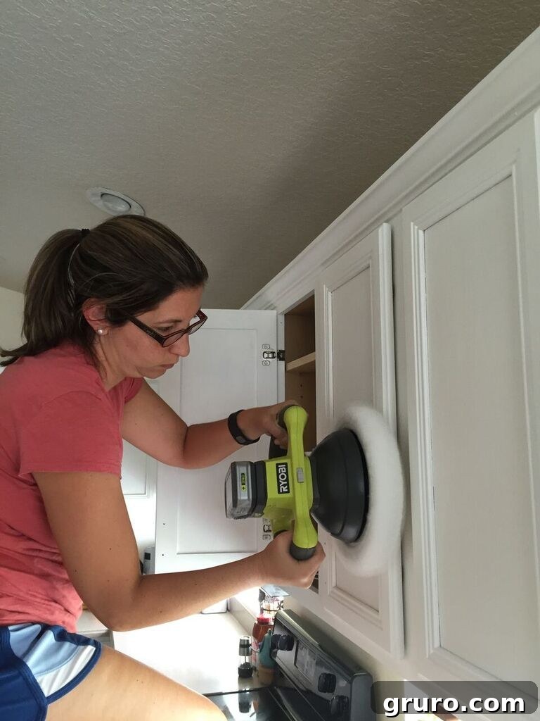 Hands buffing newly waxed kitchen cabinets with a car buffer for a smooth, professional finish